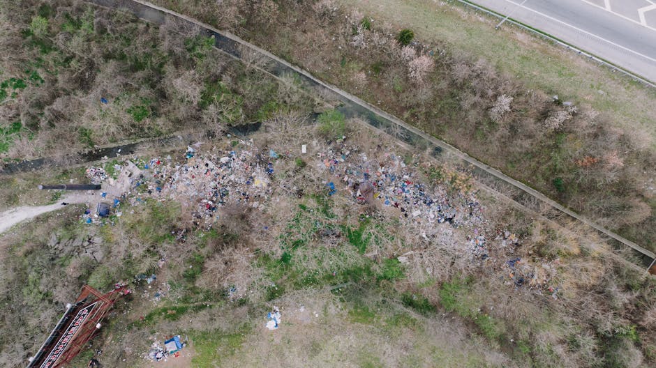 A large area of litter and waste materials, predominantly black rubber tires, discarded plastic bags, and various debris, spread across a rocky and uneven surface in the foreground. In the background,
